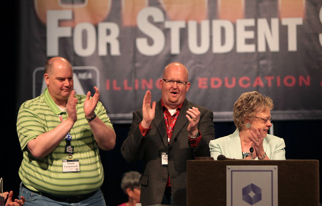 Duane Farnsworth (left) and Ben Sogergren-Baar applaud IEA President Cinda Klickna's announcement that IEA delegates had contributed more than $6200 for tornado relief.